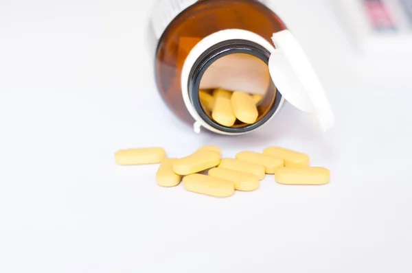 Yellow tablet from brown bottle on the white — Stock Photo, Image