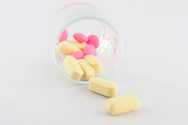 Yellow and pink tablet in dosage glass — Stock Photo, Image