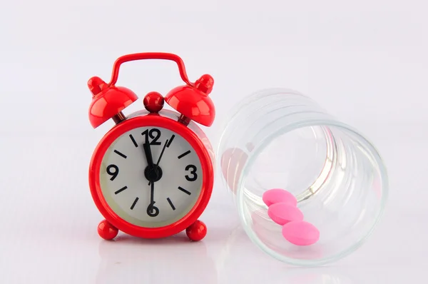 Red clock and pink tablet in dosage glass on white background — Stock Photo, Image