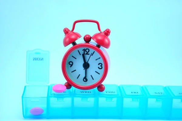 Boîte à pilules hebdomadaire et horloge rouge — Photo