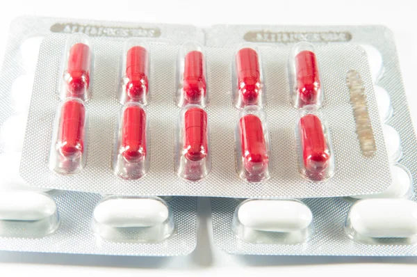Punainen kapseli läpipainopakkauksessa, valkoinen tabletti — kuvapankkivalokuva