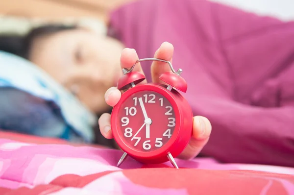 Woman snoozing a red alarm clock — Stock Photo, Image