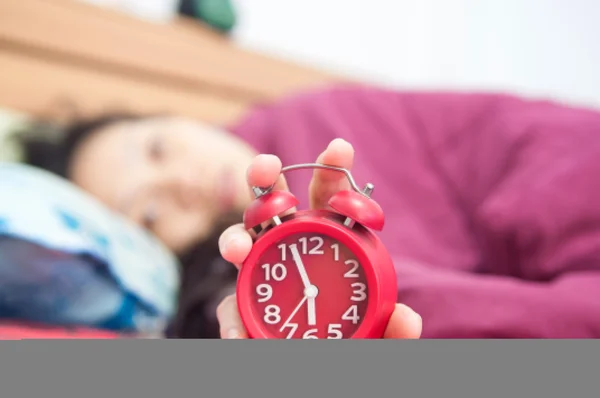 Woman snoozing a red alarm clock — Stock Photo, Image