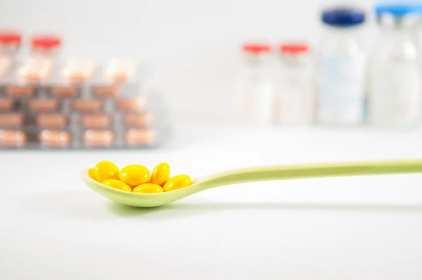 Yellow coating tablet in spoon on vial background — Stock Photo, Image