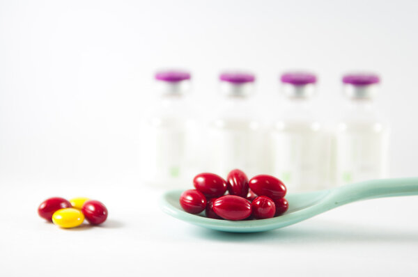 Красная таблетка в ложке на фоне лекарственных флаконов
