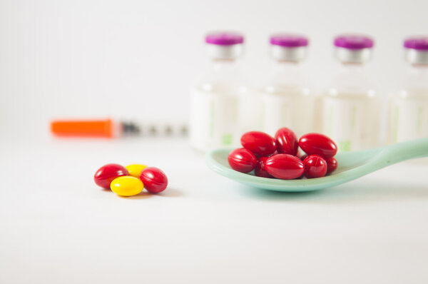 Красная таблетка в ложке на фоне лекарственных флаконов
