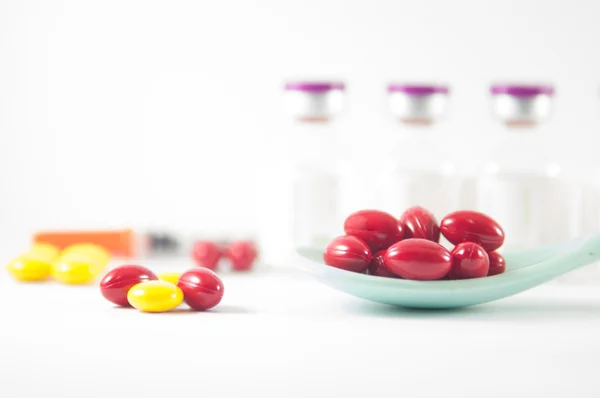 Красная таблетка в ложке на фоне лекарственных флаконов — стоковое фото