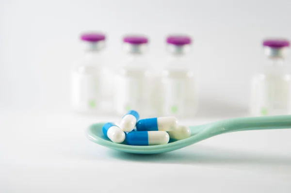 Blå och vit kapsel i sked på medicin flaskor bakgrund — Stockfoto