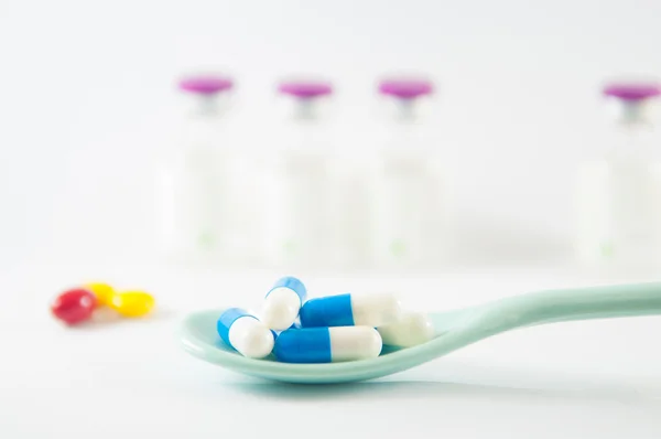 Синяя и белая капсула в ложке на фоне лекарственных флаконов — стоковое фото