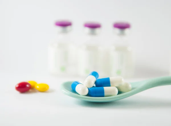 Синяя и белая капсула в ложке на фоне лекарственных флаконов — стоковое фото