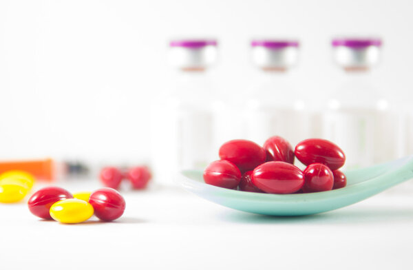 Красная таблетка в ложке на фоне лекарственных флаконов
