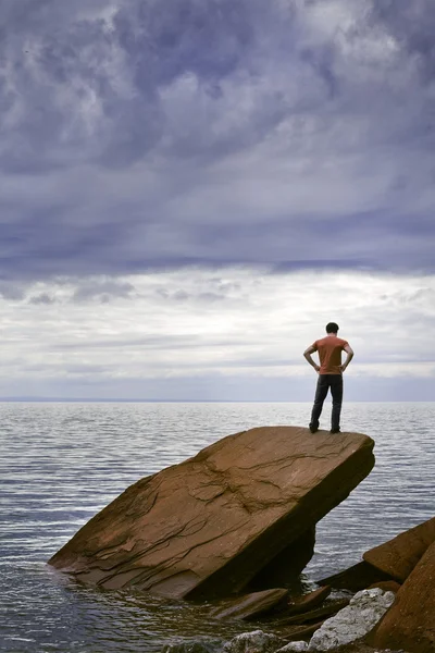 A young man stands on a rock by the sea — Stock Photo, Image