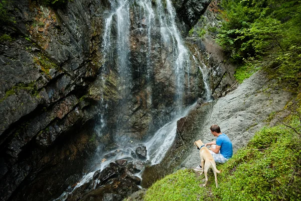 Young man with a dog near a waterfall — Stock Photo, Image