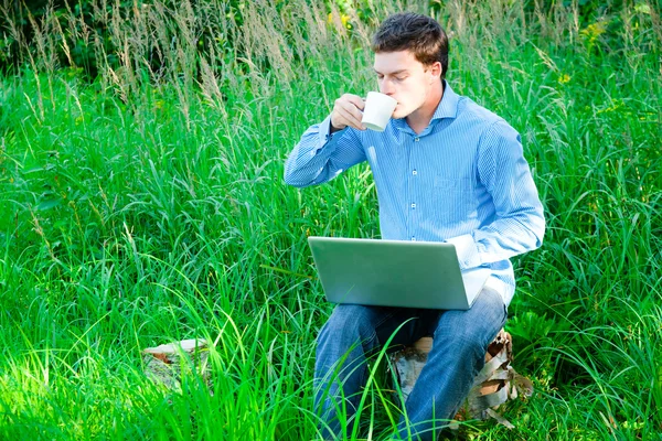Hombre joven al aire libre con una taza y un ordenador portátil —  Fotos de Stock