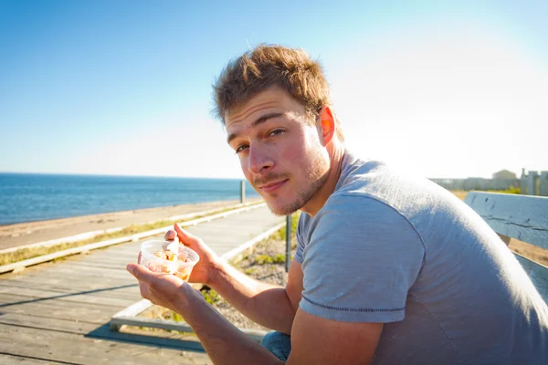Młody człowiek jedzenie na plaży — Zdjęcie stockowe