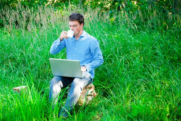 Jovem ao ar livre com uma xícara e laptop — Fotografia de Stock