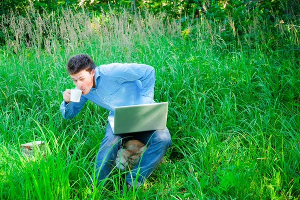 Jovem ao ar livre com uma xícara e laptop — Fotografia de Stock