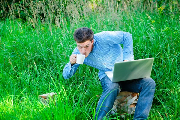 Jovem ao ar livre com uma xícara e laptop — Fotografia de Stock