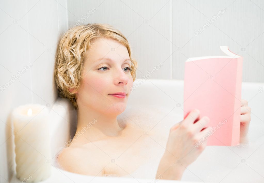 Happy young woman relaxing and reading a book in the bath