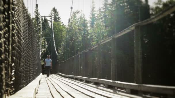 Jovem adulto caminhando em uma ponte suspensa — Vídeo de Stock