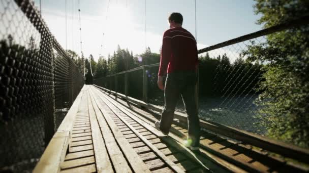 Hombre adulto joven caminando sobre un puente colgante — Vídeo de stock