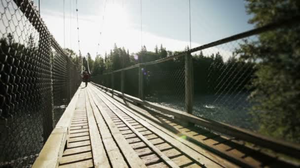 Hombre adulto joven caminando sobre un puente colgante — Vídeo de stock