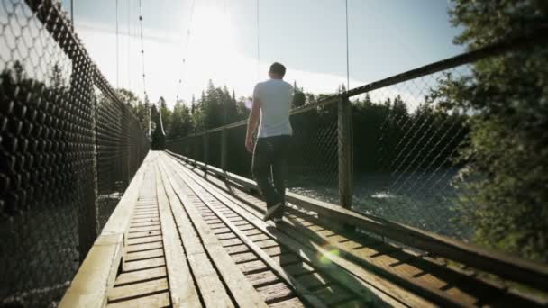 Hombre adulto joven caminando sobre un puente colgante — Vídeos de Stock