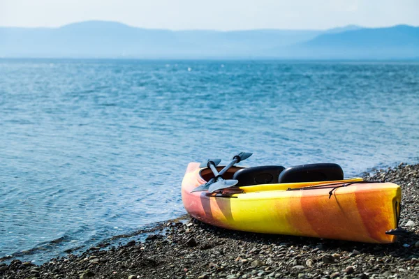 Kayak naranja y amarillo con remos en la orilla del mar —  Fotos de Stock
