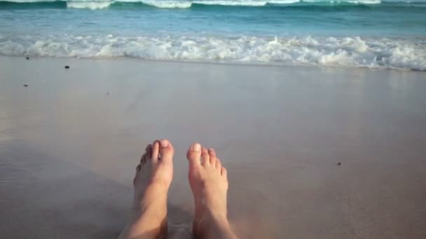 Meisje, zittend op het strand en het krijgen van haar voeten nat vanwege een golf — Stockvideo