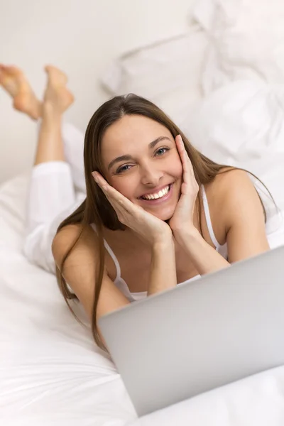 Retrato de uma jovem mulher com seu computador na cama — Fotografia de Stock