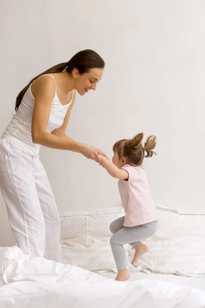 A little girl jumps on the bed with her mom — Stock Photo, Image