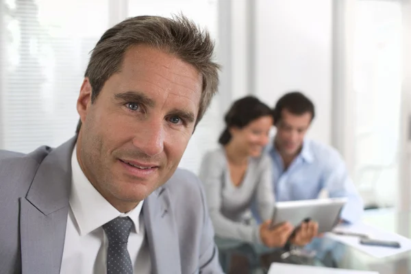 Uomo d'affari di successo in piedi con il suo personale in background presso l'ufficio in una riunione — Foto Stock