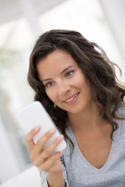 Портрет счастливой милой женщины с мобильным телефоном, сидящим на диване — стоковое фото