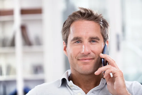 Portrait of a man using a cell phone while sitting on a sofa at — Stock Photo, Image