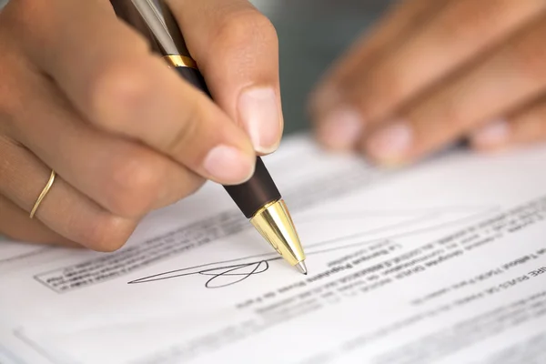 Woman at office desk signing a contract with shallow focus on si — Stock Photo, Image