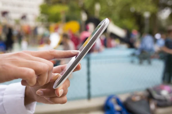 Primer plano de las manos de la mujer utilizando su teléfono celular fondo playgrou — Foto de Stock