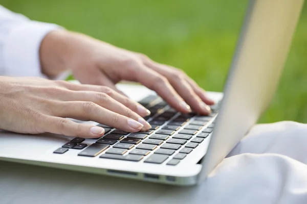 Mulher mãos digitando em um teclado laptop, fundo de grama — Fotografia de Stock