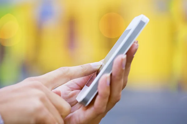 Mobile phone in a woman's hand, yellow store backgroun — Stock Photo, Image