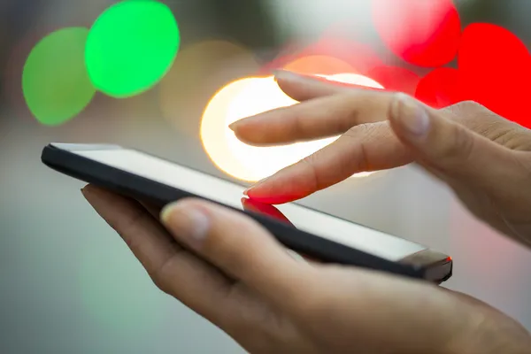 Teléfono móvil en la mano de una mujer, luces nocturnas de la ciudad — Foto de Stock