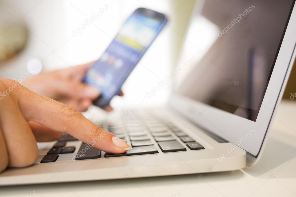 Woman hands with smart phone and computer keyboard