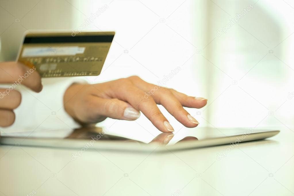 Close-up woman's hands holding a credit card and using tablet pc