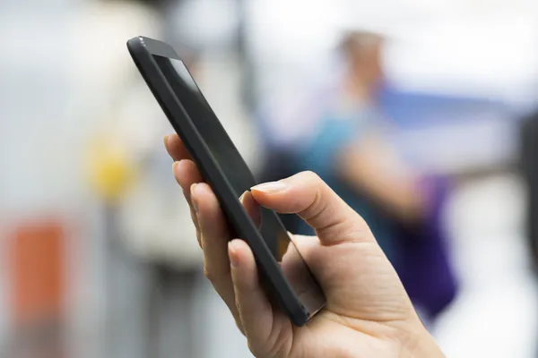 Cierre de manos mujer usando su teléfono celular en una estación de tren — Foto de Stock