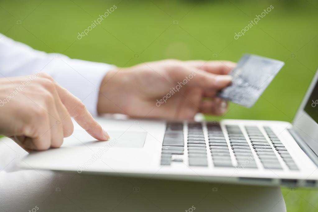Close-up woman's hands holding a credit card and using computer