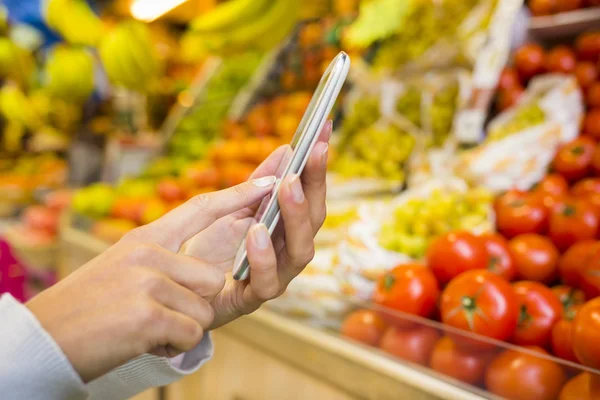 Kobieta korzystająca z telefonu komórkowego podczas zakupów w supermarkecie — Zdjęcie stockowe