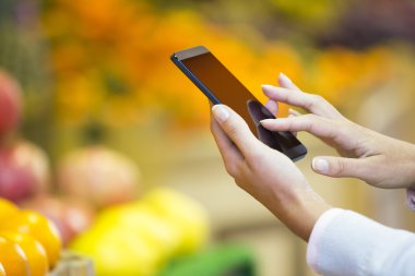 Kadın süpermarkette alışveriş yaparken cep telefonu kullanıyor