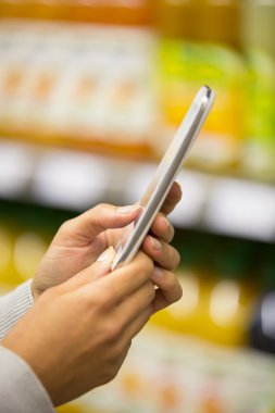 Kadın süpermarkette alışveriş yaparken cep telefonu kullanıyor