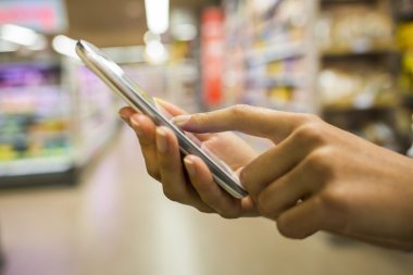 Kadın süpermarkette alışveriş yaparken cep telefonu kullanıyor