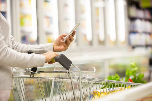 Frau benutzt Handy beim Einkaufen im Supermarkt — Stockfoto