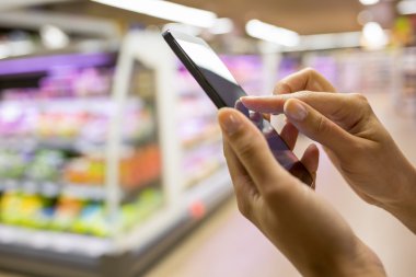 Kadın süpermarkette alışveriş yaparken cep telefonu kullanıyor