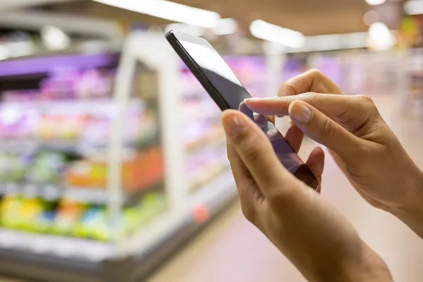 Жінка використовує мобільний телефон під час покупок у супермаркеті — стокове фото